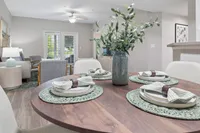 Inviting open-plan living and dining area with elegant wooden dining table, modern seating, and vibrant greenery centerpiece overlooking a serene outdoor view.