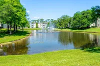 Tranquil apartment complex surrounded by lush greenery and a serene pond with elegant fountains.