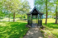 Charming wooden gazebo overlooking a tranquil pond in a lush green park setting, perfect for relaxation.