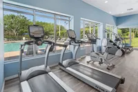 Bright fitness center with modern exercise equipment overlooking a sparkling pool and lush greenery.
