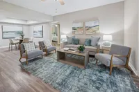 Elegant living room featuring modern furniture, accent chairs, and decorative art pieces, seamlessly connecting to a stylish dining area with contemporary artwork.