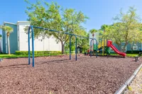 Vibrant playground in a lush residential area, featuring swings and a colorful slide set against a backdrop of green trees and modern apartments.