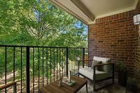 Charming balcony with cozy seating overlooking lush greenery, framed by elegant brick walls.