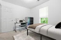 Inviting bedroom with a cozy twin bed, modern desk complete with a laptop, and ample natural light streaming through a large window.