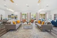 Elegant living room with modern decor, featuring chic sofas, vibrant pillows, and large windows with patterned curtains flooding the space with natural light. A pool table and stylish seating make it perfect for entertaining.