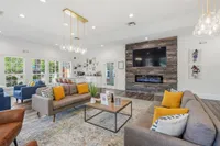 Elegant living area with modern sofas, vibrant yellow accents, a chic stone fireplace, and a large mounted TV, offering a welcoming ambiance and style.