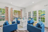 Bright and inviting living space with large windows, vibrant blue seating, and patterned curtains overlooking a lush outdoor view.
