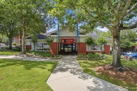 Charming apartment building entrance with vibrant landscaping and lush greenery on a sunny day, featuring a welcoming path leading to stylish brick architecture.
