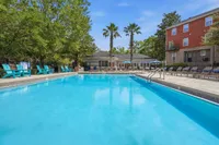 Inviting apartment community pool area with vibrant blue water, surrounded by lush greenery and comfortable seating, perfect for relaxation and socializing.
