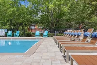 Inviting swimming pool area with stylish sun loungers and vibrant teal chairs, surrounded by lush greenery for a serene escape.