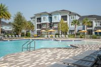 Luxurious apartment complex with beautiful poolside setting, surrounded by lush palm trees and stylish outdoor seating.