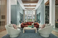 Elegant lounge area with modern design, featuring plush seating, a central table with decor, and expansive windows overlooking lush greenery.