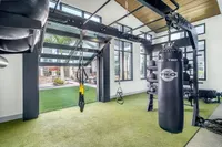 Bright and inviting fitness room featuring a modern punching bag, TRX suspension trainers, and ample natural light with a view to an outdoor relaxation area.