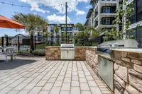 Elegant outdoor patio with modern grills, stylish stone countertops, and lush landscaping in a vibrant apartment complex.