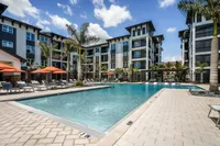 Luxurious apartment complex featuring a shimmering resort-style pool, elegant palm trees, and stylish sun loungers under vibrant orange umbrellas.