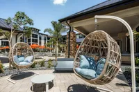 Luxury outdoor lounge with hanging egg chairs and vibrant poolside atmosphere, featuring sleek architecture and tropical landscaping.
