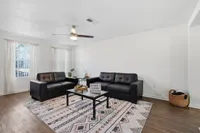 Modern living room with chic black leather sofas, a stylish geometric rug, and natural light filtering through sheer curtains.