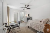 Bright and inviting bedroom with plush carpeting, a modern ceiling fan, and an en-suite bathroom. Includes a sleek glass desk for productive workspace.