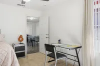 Bright, cozy bedroom with a modern glass desk and an open doorway leading to a stylish dining area.