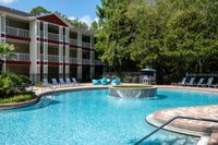 Inviting apartment complex featuring a sparkling outdoor pool with stylish lounge chairs and a serene garden backdrop.