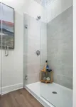 Elegant modern shower with sleek gray tiles, glass door, and stylish wooden shelf enhancing the bathroom's sophistication.