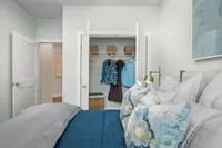 Inviting bedroom with a cozy bed adorned with textured pillows, open closet with stylish clothes, and elegant wicker storage baskets.