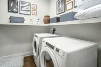 Modern laundry room featuring sleek white washer and dryer, stylish storage bins, and elegant wall art.