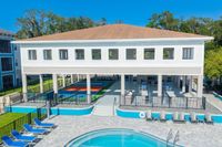 Modern apartment complex with a scenic outdoor space featuring a pristine pool, sun loungers, and multi-use sports courts, perfect for relaxation and recreation.