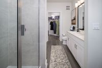 Elegant bathroom showcasing a modern glass shower, sleek white vanity with dual sinks, and walk-in closet for ample storage.