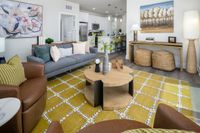 Inviting living room with modern decor, featuring a cozy gray sofa, stylish armchairs, and an elegant coffee table on a chic patterned rug, leading into a bright and open kitchen.
