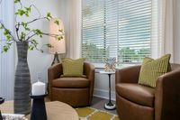 Cozy living room corner with elegant brown leather chairs, stylish greenery in a modern vase, and warm natural light streaming through blinds.