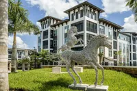 Contemporary apartment complex surrounded by lush greenery, featuring striking horse sculptures and modern architectural design.