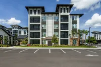 Modern apartment complex with sleek architecture, featuring spacious balconies and lush landscaping under a bright blue sky.