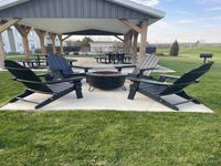 Relax and unwind at our outdoor fireside lounge. Charming outdoor area with Adirondack chairs around a fire pit under a cozy pavilion, surrounded by lush green grass and picnic tables.