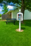 Discover a community that shares more than just good vibes! Our Little Free Library encourages residents to take a book, leave a book, and enjoy moments of connection right in the heart of the neighborhood Charming outdoor scene featuring a free-standing book exchange under a lush tree, surrounded by vibrant greenery and a cozy bench for outdoor reading enjoyment.