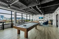 Modern apartment lounge with pool table, cozy seating area, and panoramic city views in an industrial-chic ambiance.