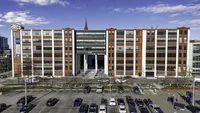 Historic industrial-style building showcasing expansive windows and modern design, with an inviting parking area under a bright blue sky.