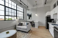 Bright and modern apartment interior with large industrial-style windows, cozy seating area, and sleek kitchen design.