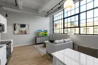 Bright and modern living space with large industrial-style windows, cozy gray sofa, and elegant decor, perfect for urban living.