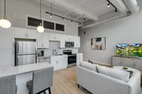 Modern open-plan kitchen and living room featuring sleek white cabinets, stainless steel appliances, and cozy seating, perfect for stylish urban living.