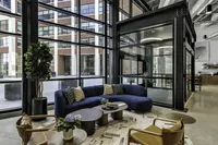 Chic and modern lobby lounge with large windows, featuring a deep blue sofa, stylish coffee tables, and indoor plants, creating an inviting and contemporary atmosphere.