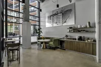 Chic industrial-style lounge with large windows, a cozy green velvet booth, modern art, and sleek shelving.