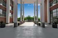 Modern apartment entrance with tall columns, large windows, and lush greenery against a bright blue sky.