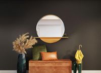 mud room wooden chest with pillows. round mirror on wall. vase with plant on left side of wooden chair, rainboots and umbrella on the right side of wooden chair