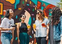 friends enjoying drinks outside in front of a painted mural