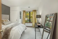 Cozy bedroom with stylish decor, featuring a plush bed, large window with lush views, elegant mirror, and chic lighting.