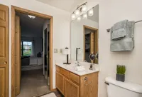 Bright and modern bathroom with elegant lighting, wooden cabinetry, and a glimpse of a cozy bedroom through the open door.