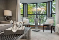 Chic living room with modern decor, large bay windows showcasing lush greenery, and cozy seating with plush cushions.