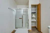 Modern bathroom with sleek glass shower, spacious linen closet, and elegant tile flooring.