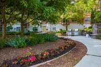 Charming garden patio with vibrant flowers, lush greenery, and modern outdoor grills, perfect for entertaining and relaxation in an upscale apartment complex.